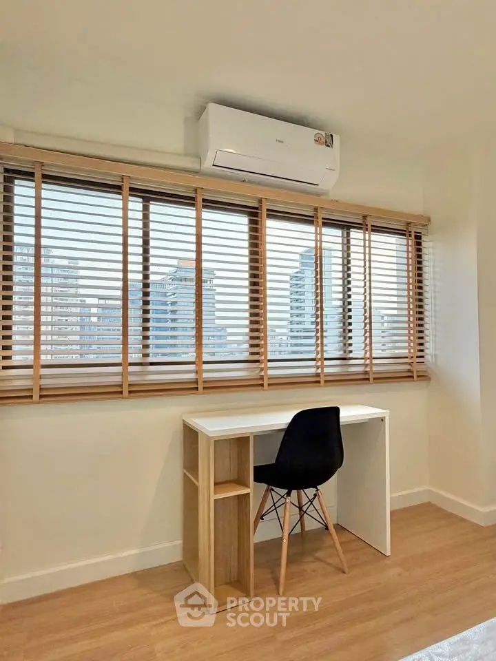 Modern study room with city view, featuring sleek desk and chair under large window with blinds.