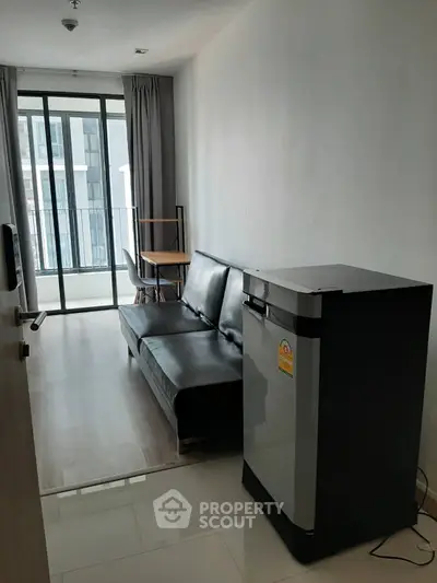 Modern living room with sleek black sofa and compact fridge, featuring floor-to-ceiling windows and balcony access.