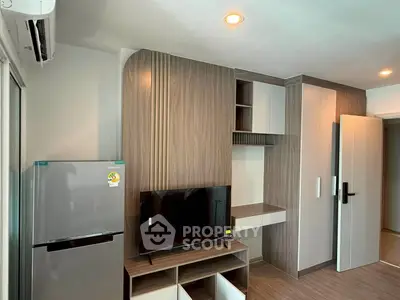 Modern living room with sleek built-in cabinets and flat-screen TV, featuring a compact refrigerator and stylish lighting.