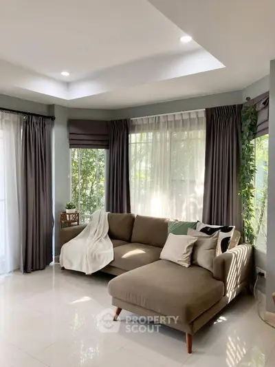 Spacious living room with modern sofa and large windows offering natural light and garden views.