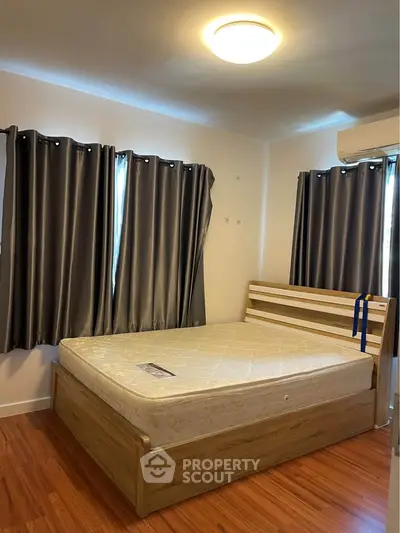 Cozy bedroom with wooden flooring and modern furnishings, featuring a comfortable bed and stylish curtains.