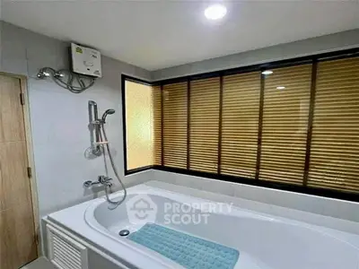 Modern bathroom with bathtub and large window with blinds