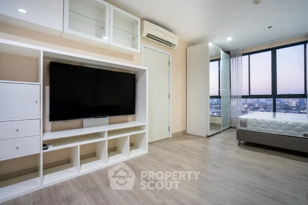 Modern bedroom with large TV and city view, featuring sleek design and natural light.