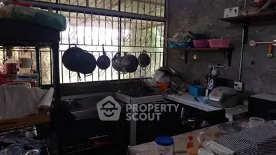Rustic kitchen with open layout and gas stove, featuring hanging pots and natural light.