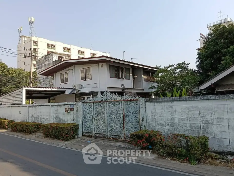 Charming two-story house with ornate gate and lush greenery in urban setting