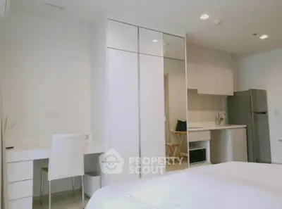 Modern bedroom with sleek white furniture and compact kitchen area, perfect for urban living.