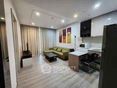 Modern living room with stylish decor and open kitchen layout, featuring a cozy green sofa and sleek appliances.