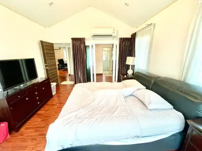Spacious bedroom with modern decor and large bed, featuring a flat-screen TV and elegant wooden flooring.