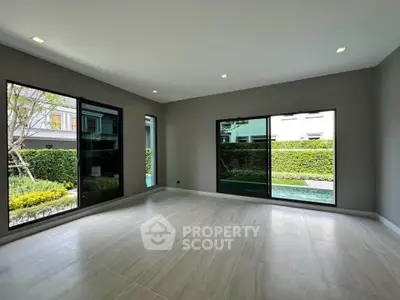 Spacious modern living room with large windows overlooking lush garden and pool area.