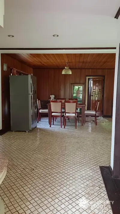 Charming rustic dining area with wooden paneling and modern fridge, perfect for cozy family gatherings.