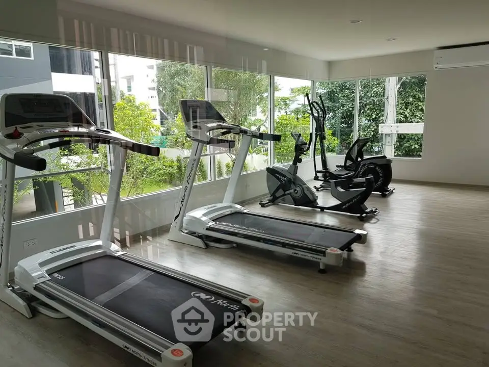 Modern gym with treadmills and exercise bikes in a bright, spacious room with large windows.
