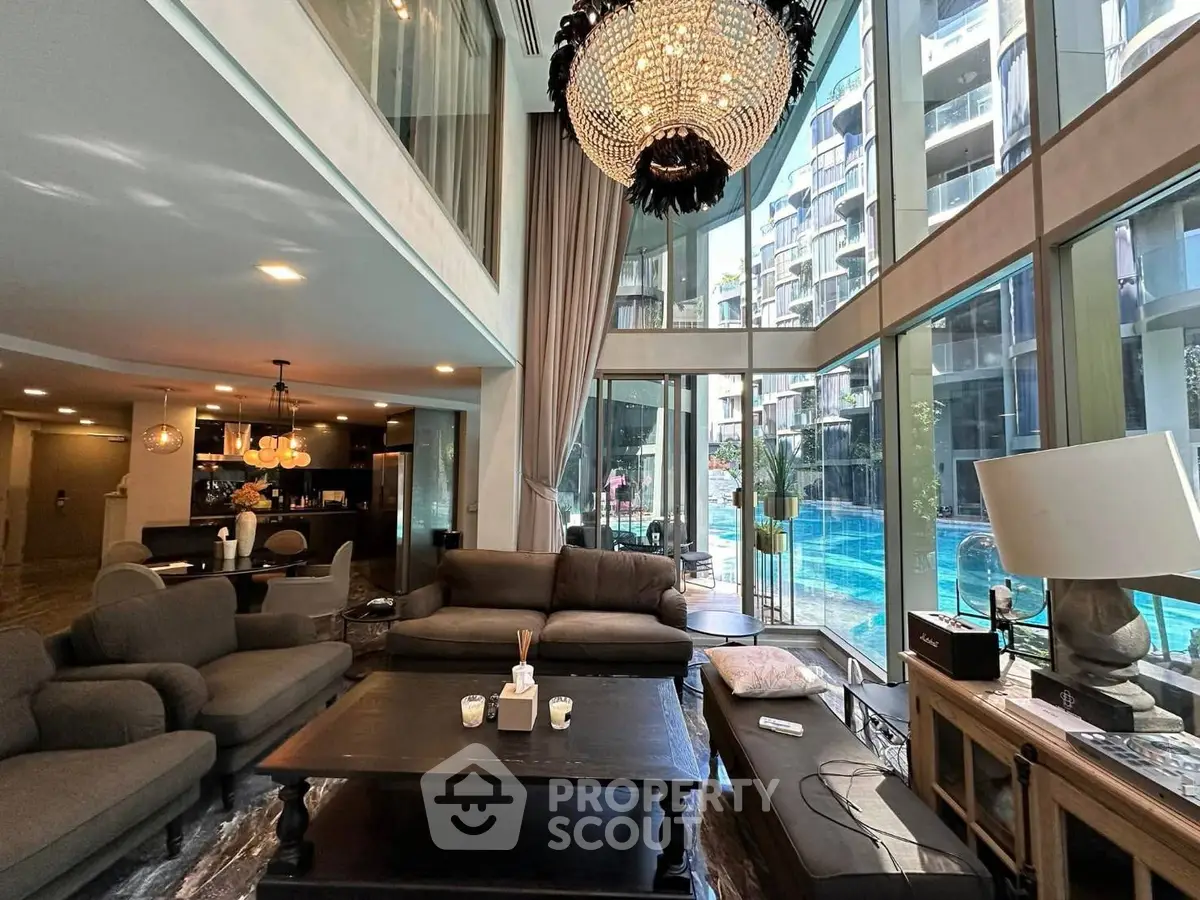 Luxurious living room with floor-to-ceiling windows overlooking a stunning pool view, featuring elegant decor and chandelier.