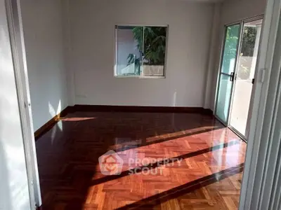 Spacious empty room with polished wooden floors and large windows offering natural light.