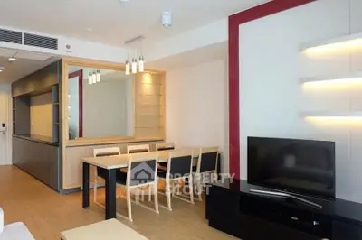 Modern living room with sleek furniture and open dining area, featuring a large TV and stylish lighting.