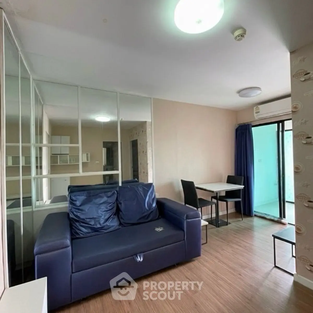 Modern living room with blue sofa and dining area, featuring mirrored wall and balcony access.