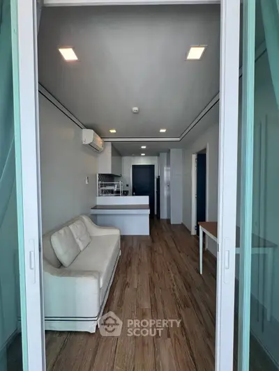 Modern open-layout living room with sleek kitchen and cozy sofa, featuring stylish wood flooring.