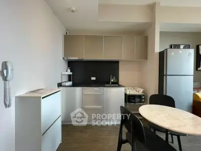 Modern kitchen with sleek cabinets, dining table, and stainless steel appliances in a cozy apartment.