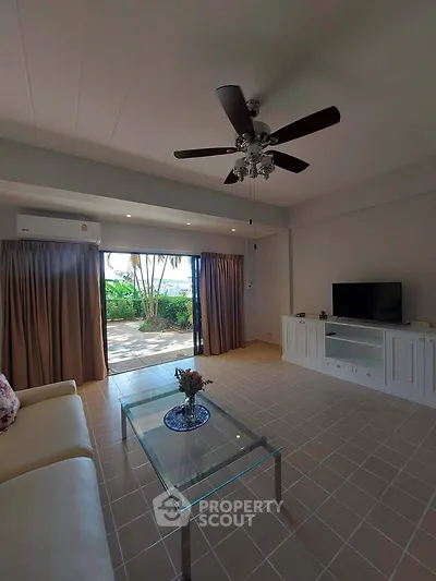 Spacious living room with modern decor and garden view, featuring a ceiling fan and glass coffee table.