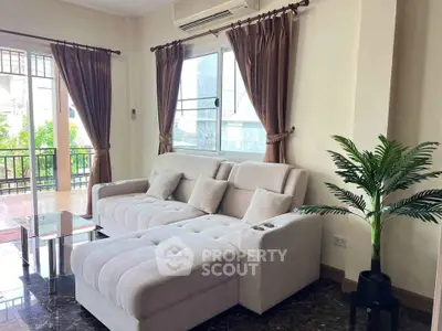 Spacious living room with plush sofa and large windows opening to a balcony, perfect for relaxation.