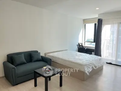 Modern studio apartment with bed, sofa, and large window offering natural light.