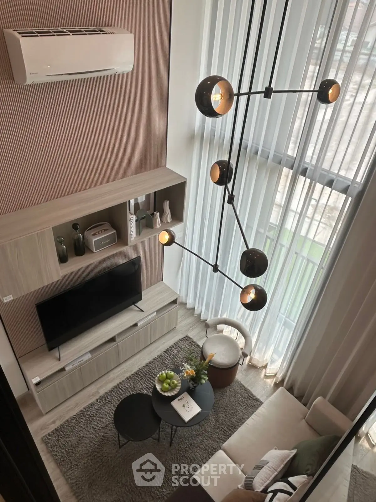 Modern living room with high ceiling and stylish lighting, featuring a cozy seating area and large windows.