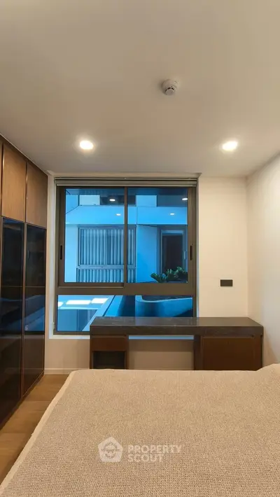 Modern bedroom with large window and built-in wardrobe overlooking urban view.