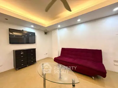 Modern living room with stylish red sofa and glass coffee table, featuring recessed lighting and wall-mounted TV.