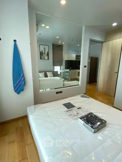 Modern bedroom with wooden flooring and large mirror reflecting a stylish living area.