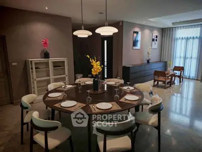 Elegant dining room with modern decor and large round table set for dinner, featuring stylish lighting and contemporary furnishings.