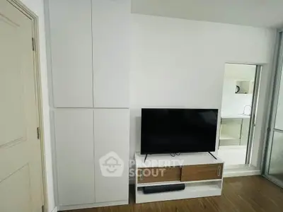 Modern living room with sleek TV stand and minimalist decor, adjacent to a compact kitchen area.