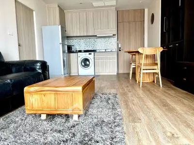 Modern open-plan living room with kitchen, featuring wooden furniture and sleek appliances.