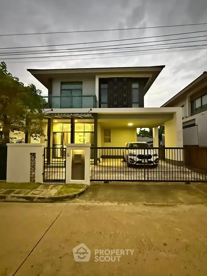 Modern two-story house with carport and gated entrance at dusk.