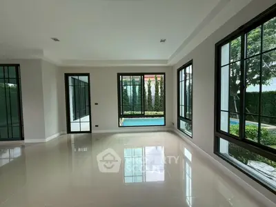 Spacious living room with large windows overlooking a serene pool and garden.