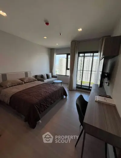 Modern bedroom with city view, featuring a cozy bed, desk, and large windows for natural light.