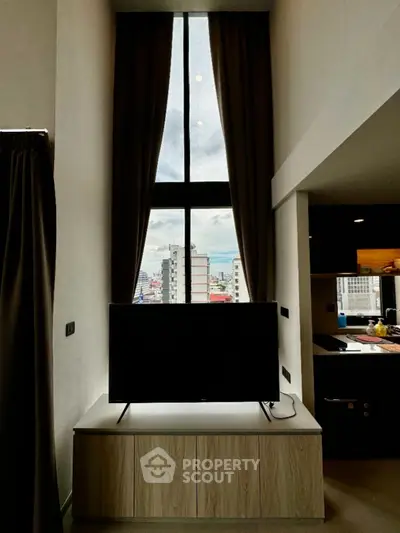 Modern living room with high ceiling and large window offering city view, featuring sleek TV setup.