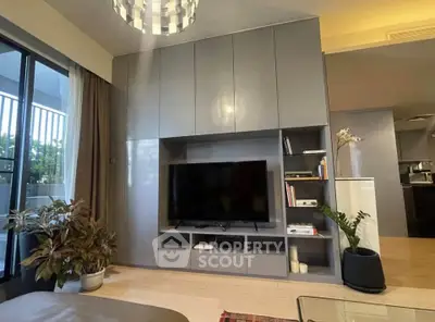 Modern living room with sleek cabinetry and large TV, featuring stylish decor and natural light.