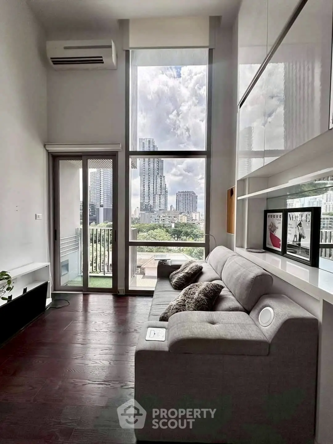 Modern living room with large windows and city view, featuring sleek furniture and high ceilings.