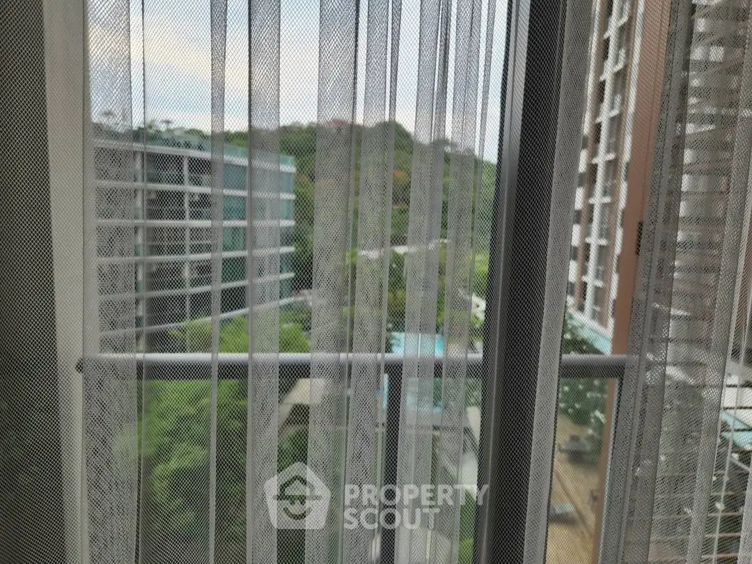 Scenic view from apartment window with sheer curtains and lush greenery