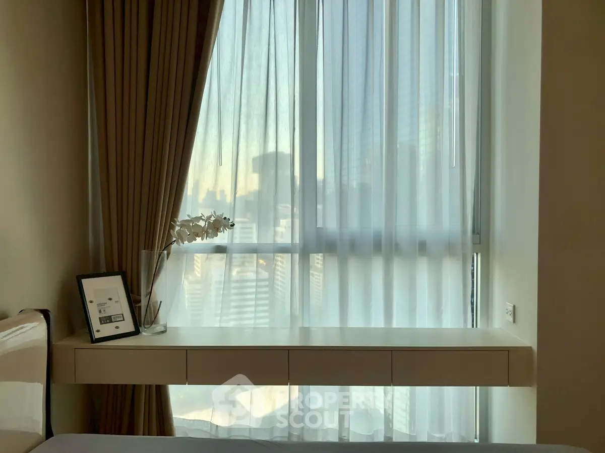 Modern bedroom with sleek floating desk and city view through large window.