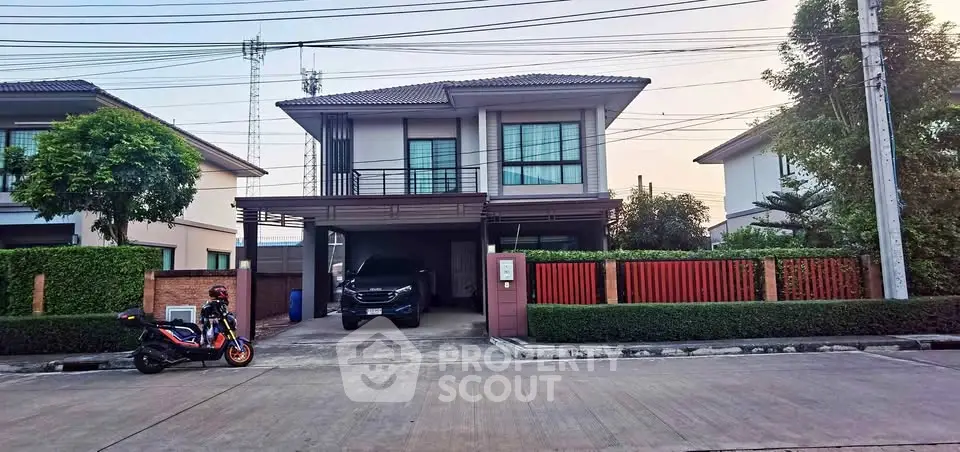 Modern two-story house with driveway and car parked, featuring sleek design and lush greenery.