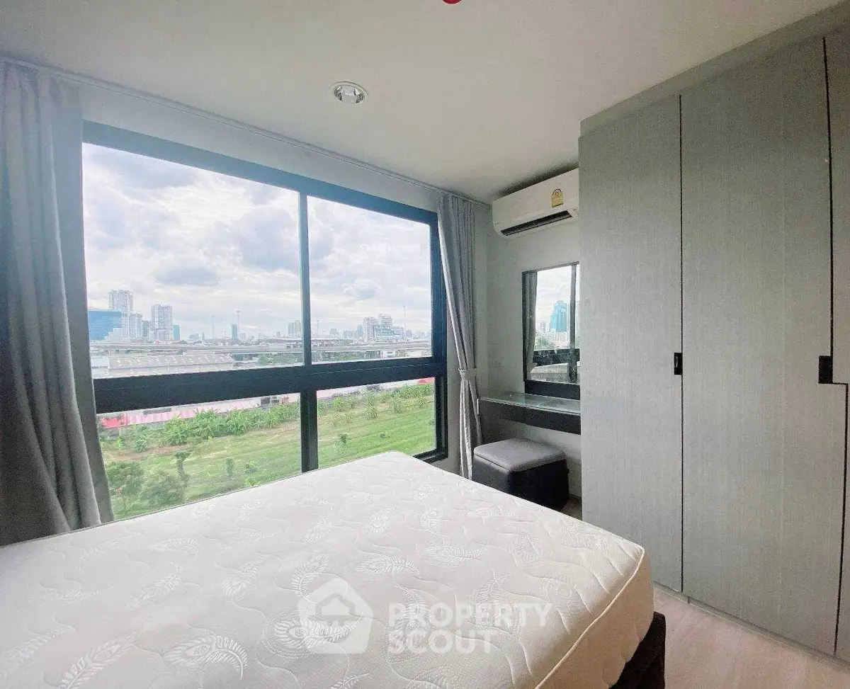 Bright bedroom with large window offering stunning city view, modern decor, and ample natural light.