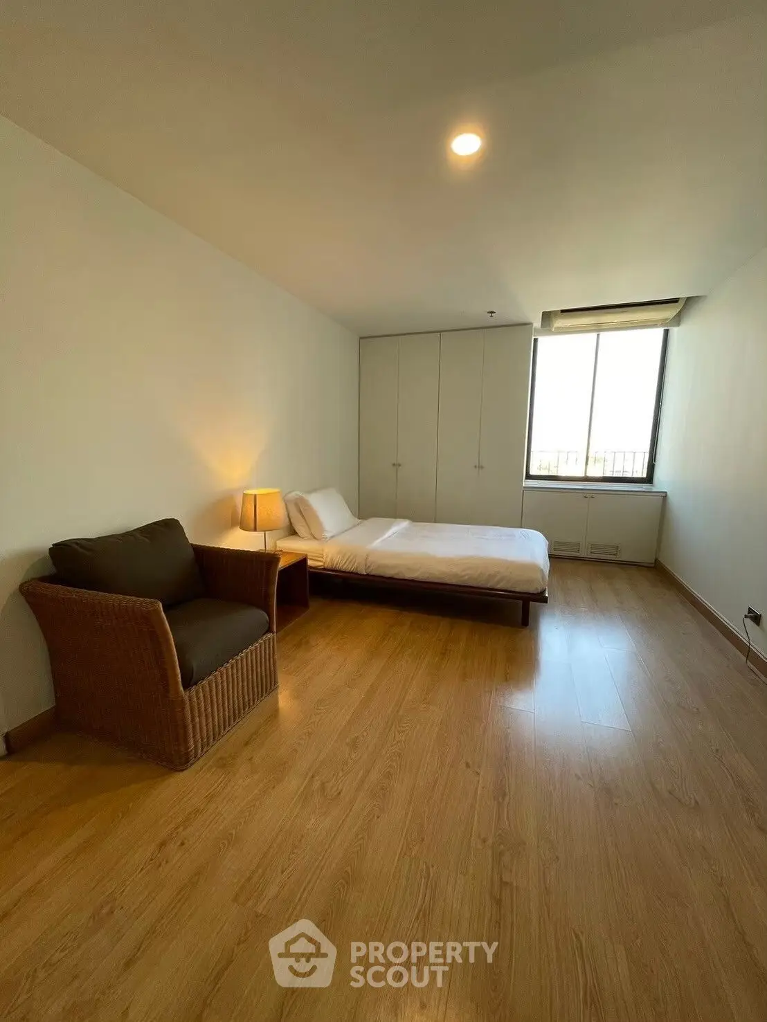 Spacious bedroom with wooden flooring and cozy wicker chair