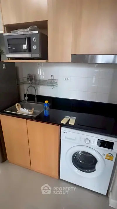 Modern kitchen with washing machine and microwave, sleek cabinetry, and compact design.