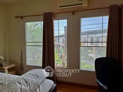 Cozy bedroom with large windows offering a serene view of the neighborhood, perfect for relaxation.