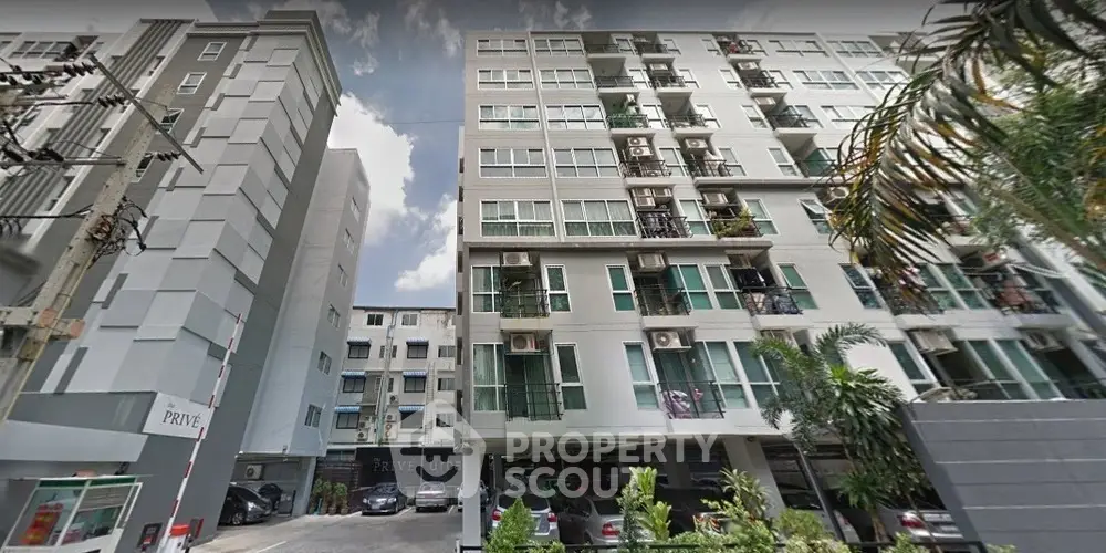 Modern urban apartment building exterior with parking area and lush greenery.