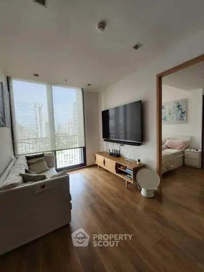 Modern living room with large TV and city view, connected to a cozy bedroom.