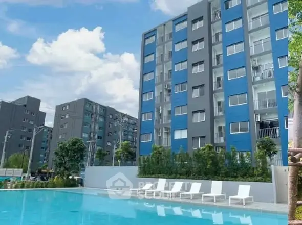 Modern apartment complex with pool and lush greenery under a clear blue sky.