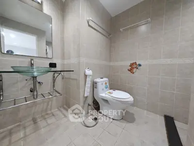 Modern bathroom with glass sink and tiled walls, featuring a decorative toilet.