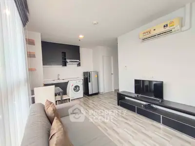 Modern living room with open kitchen, featuring a washing machine and sleek black furniture.