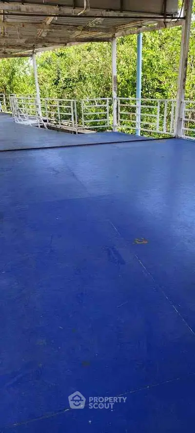 Spacious outdoor balcony with vibrant blue flooring and lush greenery view.